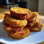 A stack of Impossibly Crispy Baked Eggplant slices with a golden-brown, crunchy coating served on a white plate.