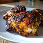 Close-up of three perfectly cooked Garam Masala Chicken Thighs with a dark, spiced, and slightly charred exterior on a white plate.