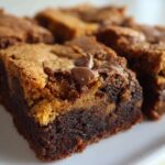 A close-up of a perfectly layered square of Brookies, showing a dense chocolate brownie base topped with a lighter cookie layer and a melted chocolate chip.