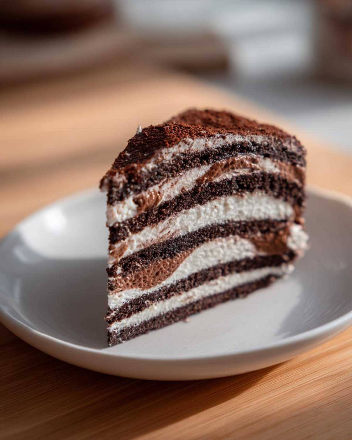 A tempting slice of Lazy Cat Cake showing alternating dark chocolate and white cream layers, dusted with cocoa.