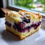 A close-up of a square slice of Lemon Blueberry Cheesecake Dump Cake showing layers of cake, creamy filling, and rich blueberries.