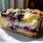 A close-up slice of Lemon Blueberry Cheesecake Dump Cake showing layers of crust, creamy cheesecake filling, and bright blueberries.