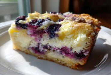 A close-up slice of Lemon Blueberry Cheesecake Dump Cake showing layers of crust, creamy cheesecake filling, and bright blueberries.