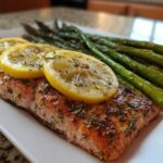 A perfectly cooked salmon fillet topped with lemon slices and herbs, served alongside roasted asparagus, demonstrating one of the High Protein Meals That Melt Belly Fat Fast.