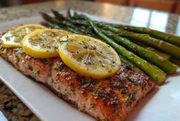 A perfectly cooked salmon fillet topped with lemon slices and herbs, served alongside roasted asparagus, demonstrating one of the High Protein Meals That Melt Belly Fat Fast.