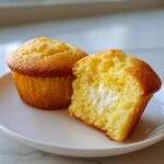 Two Lemon Muffins Cream Cheese Filling Soft on a white plate, one cut open showing the creamy center.
