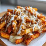 Close-up of crispy fries smothered in brown gravy, melted cheese curds, and a white sauce, resembling Louisiana Voodoo Fries.