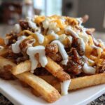 A close-up of loaded Louisiana Voodoo Fries Wingstop copycat, featuring french fries topped with gravy, cheese, and a white sauce.