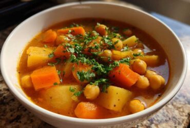 A close-up of a white bowl filled with rich, orange broth, potatoes, carrots, and chickpeas, topped with fresh parsley, showcasing Mastering Chickpea Potato Soup.