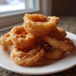 A close-up stack of golden brown, perfectly fried Onion Rings Extra Crispy resting on a white plate.