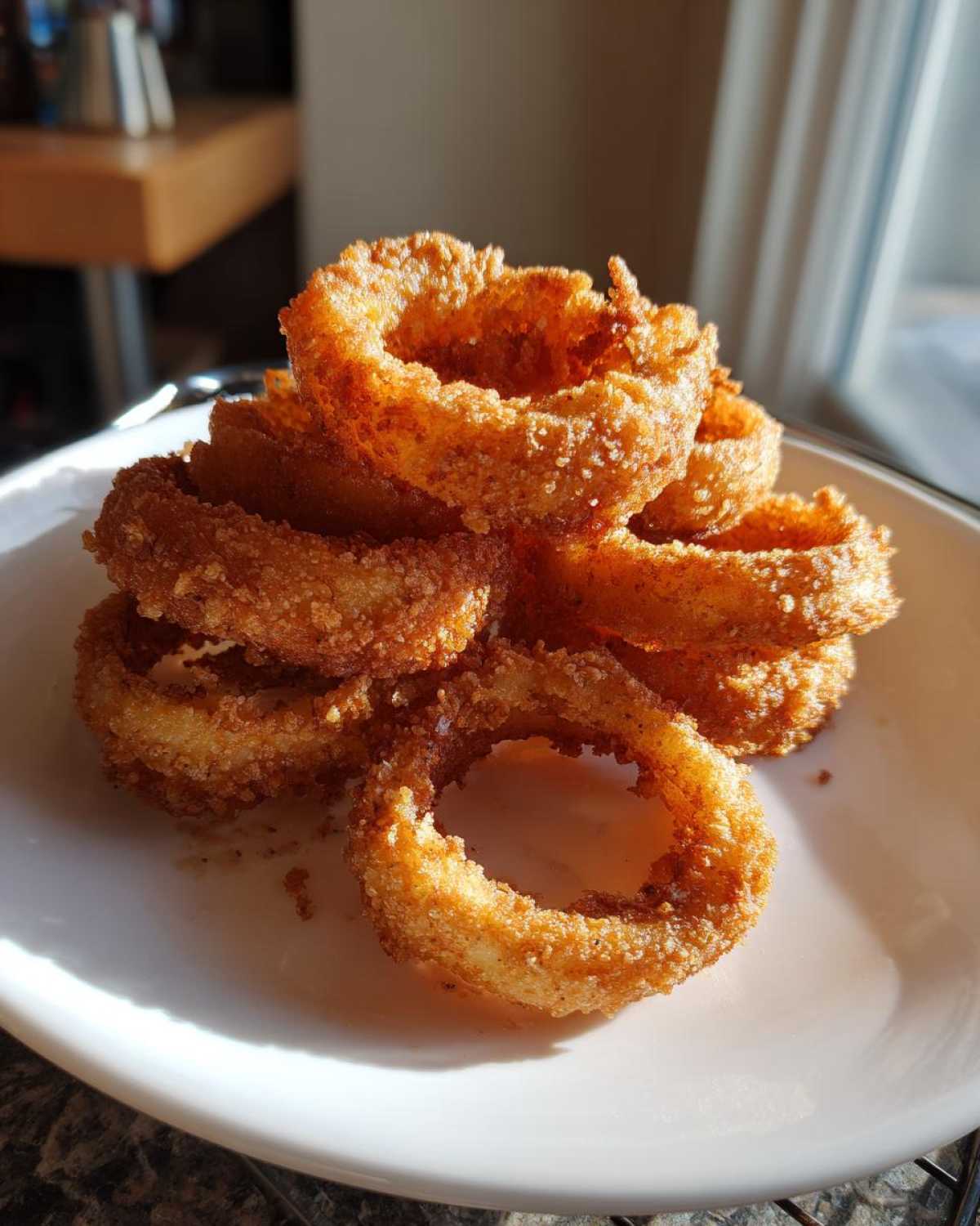 A stack of golden brown, perfectly breaded Onion Rings Extra Crispy piled high on a white plate.