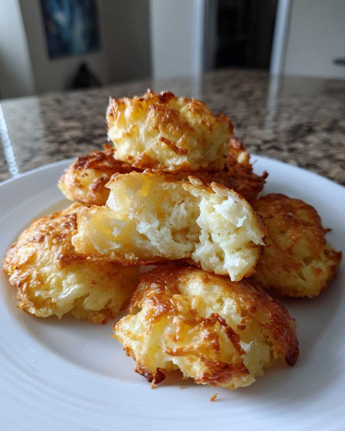 A stack of crispy Parmesan Crusted Smashed Potatoes on a white plate, one is broken open showing the fluffy interior.