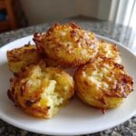 A close-up of five golden-brown Parmesan Crusted Smashed Potatoes served on a white plate.