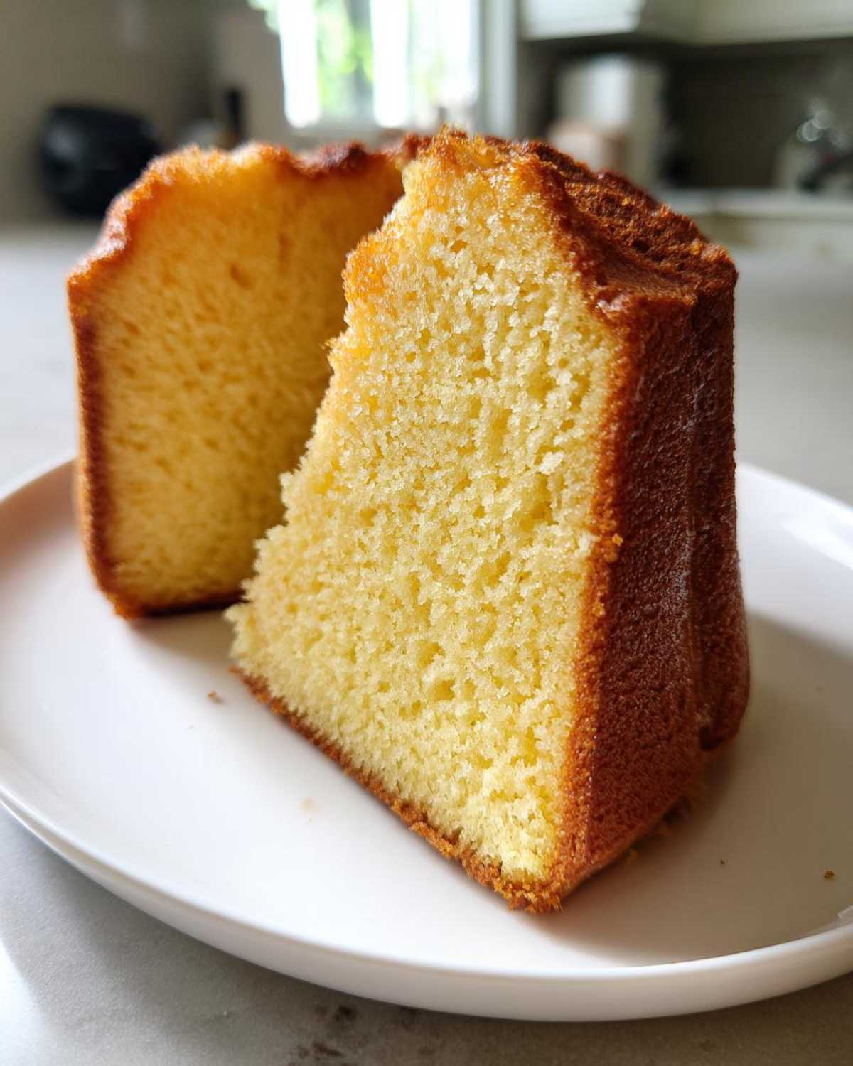 A close-up view of two slices of moist, golden pound cake sitting on a white plate.