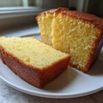 Two slices of moist, golden pound cake resting on a white plate, showcasing the dense crumb texture.