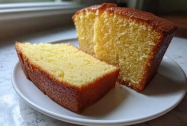 Two slices of moist, golden pound cake resting on a white plate, showcasing the dense crumb texture.