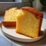 Two thick slices of golden yellow pound cake showing a dense, moist crumb texture on a light plate.