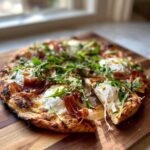 A freshly baked Prosciutto Honey Burrata Pizza topped with fresh arugula and a drizzle of honey, resting on a wooden board.