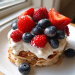 Close-up of a stack of Protein Pancake Bowls with Yogurt and Berries, topped with fresh strawberries, blueberries, and raspberries.
