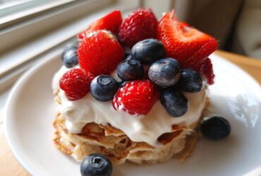 Close-up of a stack of Protein Pancake Bowls with Yogurt and Berries, topped with fresh strawberries, blueberries, and raspberries.