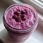 Overhead view of vibrant pink Raspberry Chia Seed Pudding topped with whole raspberries in a glass jar.