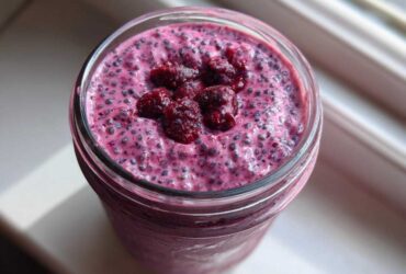 Overhead view of vibrant pink Raspberry Chia Seed Pudding topped with whole raspberries in a glass jar.