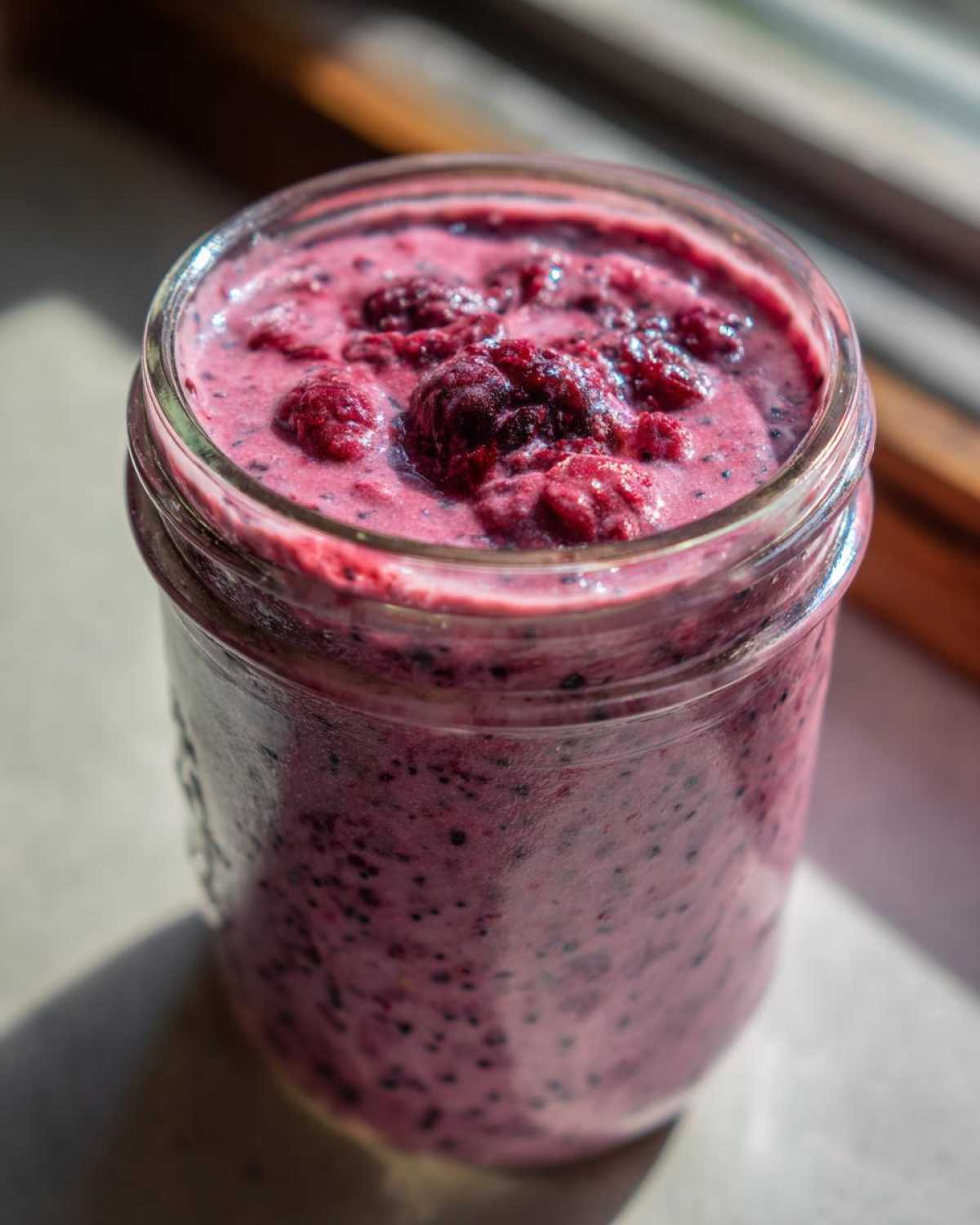 Close-up of a vibrant Raspberry Chia Seed Pudding topped with whole berries in a glass jar.