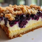 Close-up of a layered slice of Sherrys Blueberry Cream Cheese Crumb Cake showing cake base, cream cheese, blueberries, and crumb topping.