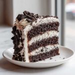 A tall, decadent slice of Cookies and Cream Cake featuring dark chocolate layers and white frosting with cookie crumbles.