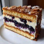 Close-up of a slice of Sherrys Blueberry Cream Cheese Crumb Cake showing layers of cake, cream cheese filling, and blueberries.
