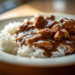 Close-up of tender chicken pieces covered in rich brown gravy served over fluffy white rice, perfect for Smothered Chicken and Rice.