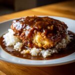 A close-up of crispy fried Smothered Chicken and Rice generously topped with rich brown gravy.