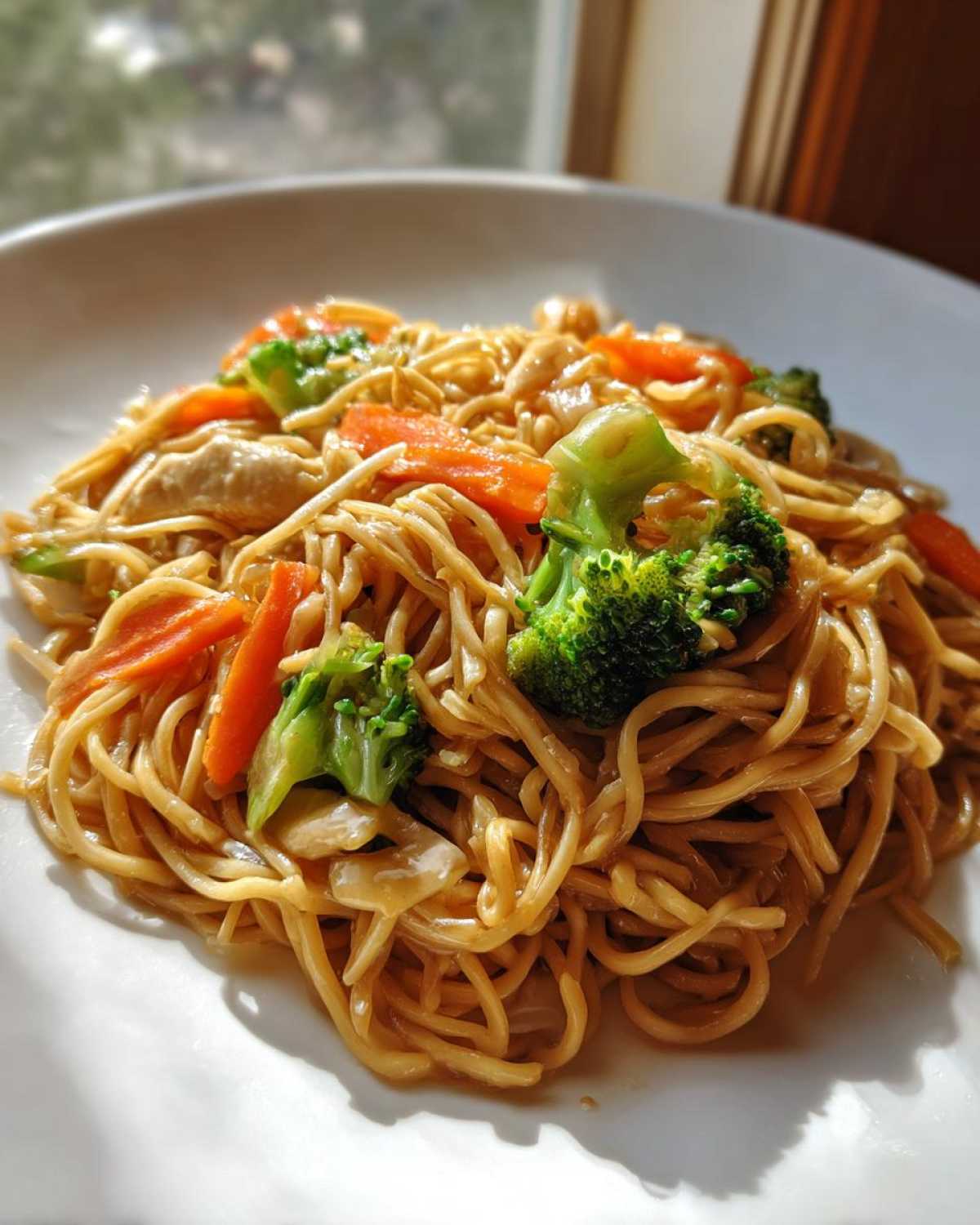 A close-up serving of Stir Fried Lo Mein noodles mixed with bright green broccoli florets and sliced carrots on a white plate.