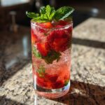 Close-up of a tall glass filled with a fizzy Strawberry Mojito Mocktail, loaded with sliced strawberries and fresh mint leaves.