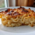 A close-up of a square serving of Tennessee Onions Gratin, showing layers of tender onions and a deeply browned, crispy topping.