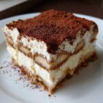 A rich slice of Tiramisu dessert, layered with cream and dusted heavily with cocoa powder, perfect for Recetas de Café.
