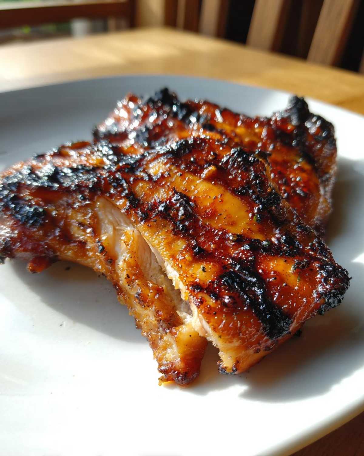 Close-up of two pieces of richly glazed and charred Vietnamese Grilled Chicken resting on a white plate.