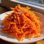 Bright orange mound of shredded carrots making up the Viral Tiktok Carrot Salad, topped with white sesame seeds.