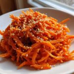 A close-up of bright orange, shredded Viral Tiktok Carrot Salad topped generously with white sesame seeds.
