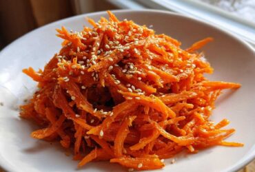 A close-up of bright orange, shredded Viral Tiktok Carrot Salad topped generously with white sesame seeds.