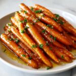 A close-up of bright orange Whiskey Glazed Carrots coated in a shiny sauce and sprinkled with chopped parsley.