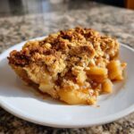A close-up of a warm slice of Apple Crisp showing gooey apples and a golden brown oat crumble topping.