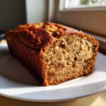 A close-up of a golden brown Apple Cinnamon Bread loaf, showing the moist crumb and visible chunks of apple and walnuts.