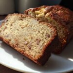Two thick slices of moist Apple Cinnamon Bread showing visible chunks of apple and a golden-brown crust, served on a white plate.