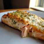 A close-up of a perfectly cooked Baked Salmon fillet topped with melted cheese and fresh herbs.