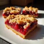 A close-up of a freshly baked Cherry Crumble Bars square showing a thick layer of bright red cherry filling beneath a crumbly topping.