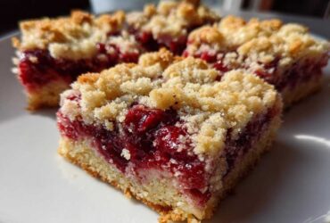 Close-up of several squares of golden Cherry Crumble Bars with a thick, bright red cherry filling and crumb topping.