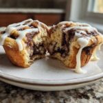 A close-up of Cinnamon Roll Muffins split in half, showing the swirl and dripping cream cheese icing.
