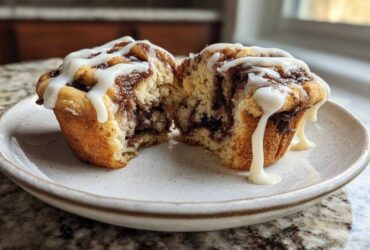 A close-up of Cinnamon Roll Muffins split in half, showing the swirl and dripping cream cheese icing.