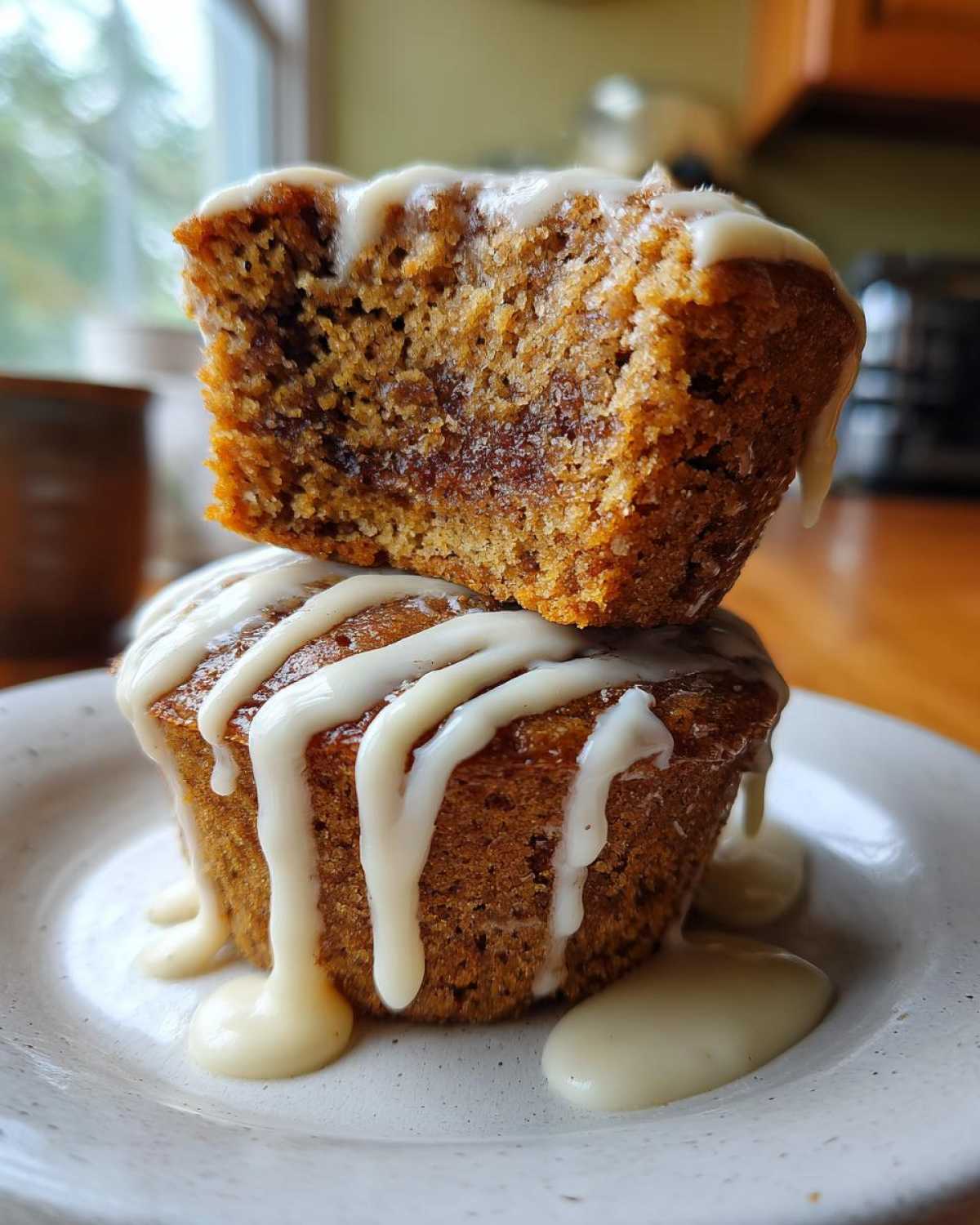 Two Cinnamon Roll Muffins stacked, one cut in half showing the swirl, drizzled heavily with white icing.